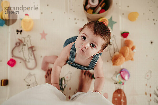 Cute baby girl standing near mother's leg on mat