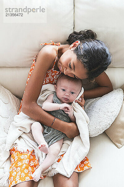 Girl embracing baby and resting on sofa at home