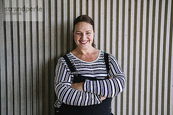 Smiling woman with arms crossed in front of textured wall