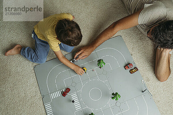 Father and son playing with toy cars on track at home