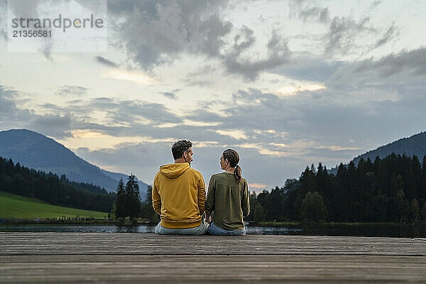 Mature man and woman looking at each other sitting on jetty