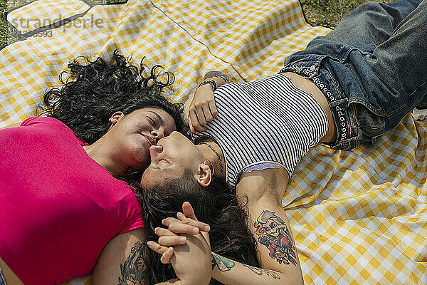 Young woman kissing girlfriend lying on picnic blanket