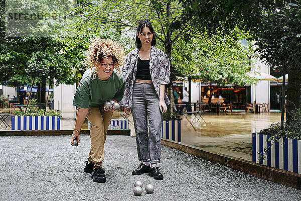 Happy young lesbian couple playing bocce balls in front of trees