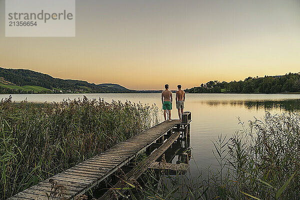 Shirtless friends standing on jetty at sunrise