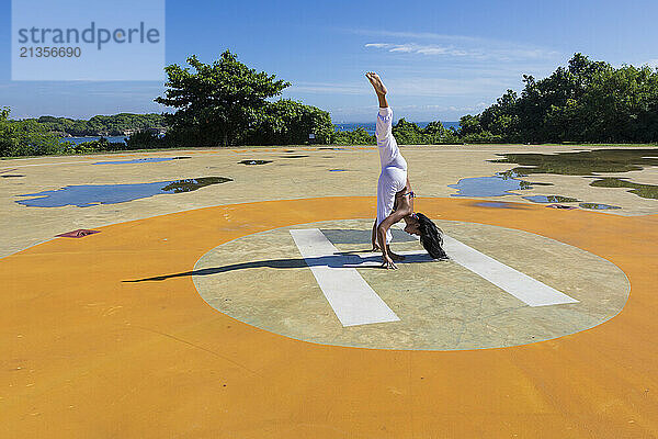 Flexible woman doing standing spilts at public park on sunny day