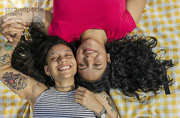 Happy young gay couple lying cheek to cheek on picnic blanket