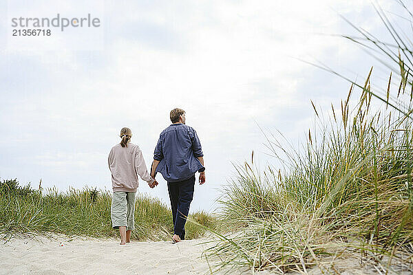 Father and daughter holding hands and walking on beach