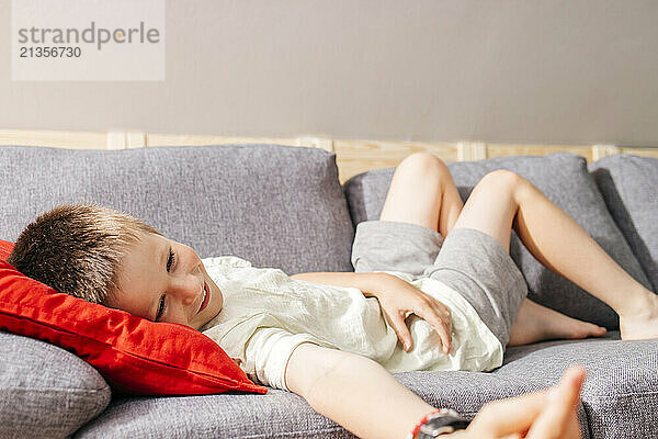 Smiling boy lying on sofa in living room at home