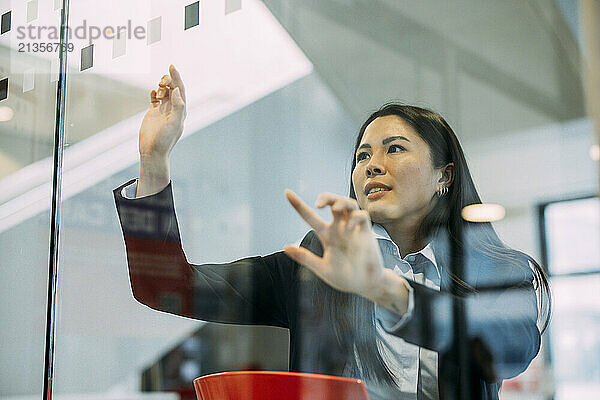 Confident businesswoman touching glass wall examining strategy at workplace