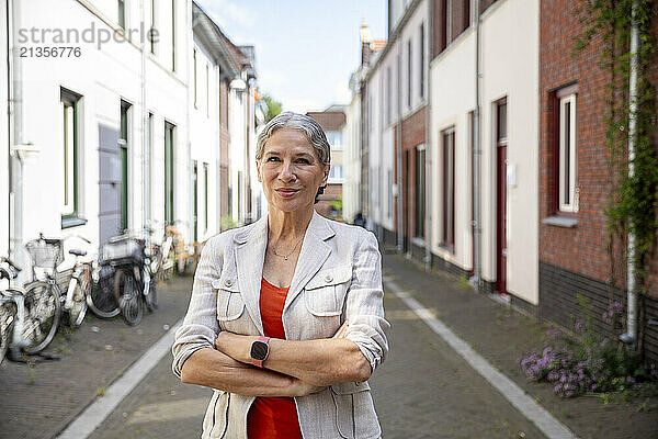 Smiling senior woman with arms crossed standing in alley