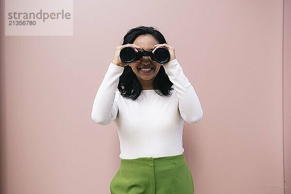 Smiling woman with binoculars near pink wall