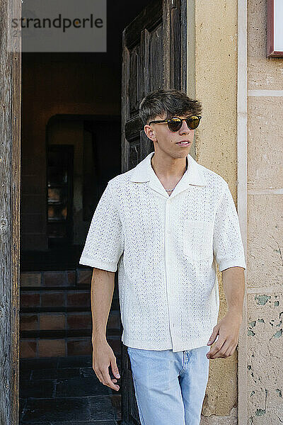 Young man wearing sunglasses and walking near doorway