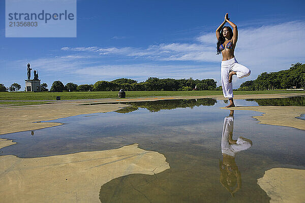 Yoga instructor doing tree pose in Bali at public park under blue sky