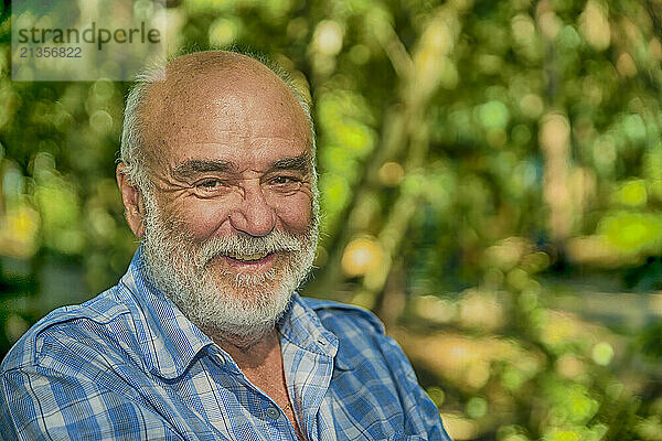 Smiling senior man with gray beard in front of trees