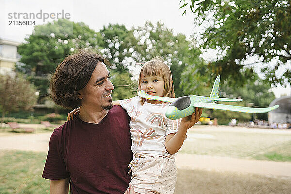 Father carrying daughter with toy plane in park