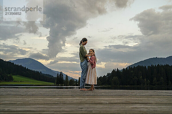 Mother and daughter standing together on jetty near mountains