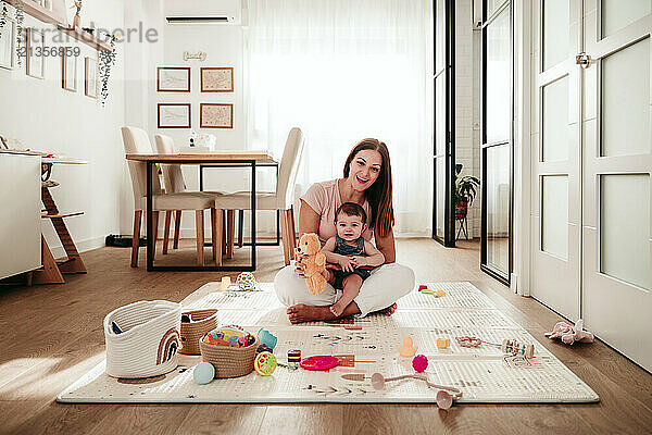 Happy woman sitting with baby daughter on rug in dining room