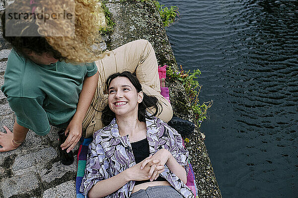 Happy woman lying with head on girlfriend's lap near river