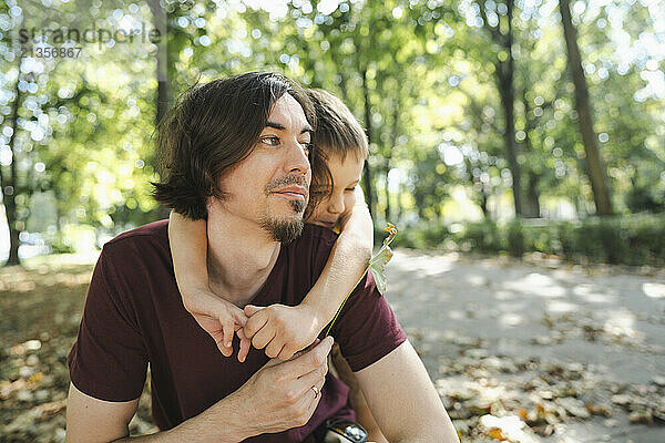 Boy hugging father from behind in park