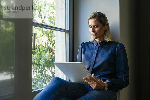 Businesswoman using tablet PC and sitting near window