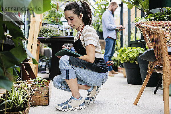 Young botanist kneeling and using tablet PC in greenhouse