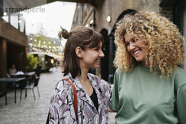 Happy lesbian couple looking at each other in front of building