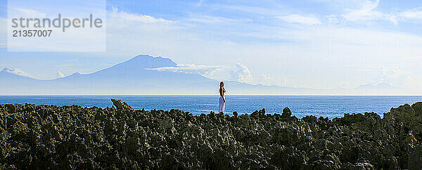 Woman standing on cliff near Nusa Dua ocean under cloudy sky