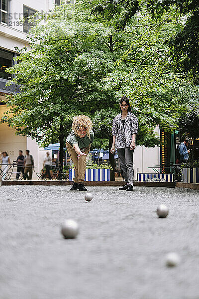 Happy lesbian couple playing boccia balls near trees