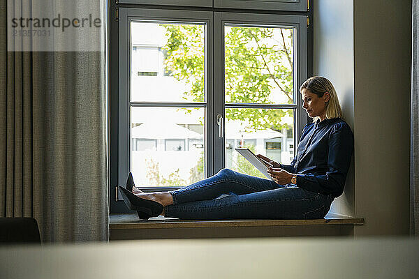 Businesswoman using tablet PC on window sill in office