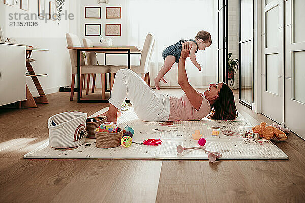 Happy mother picking up baby girl and lying down in dining room