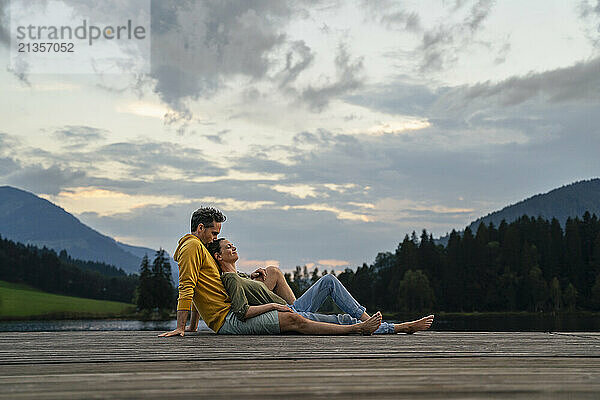 Mature man kissing woman sitting on jetty in evening