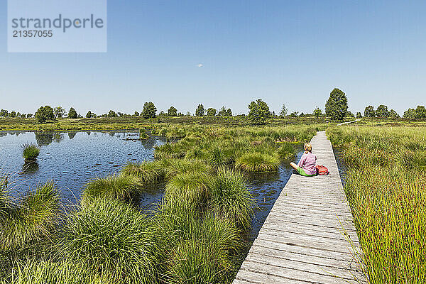 Senior woman sitting on boardwalk under sky in High Fens national park  Wallonia  Belgium