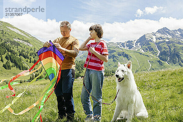 Father holding kite standing with daughter and dog