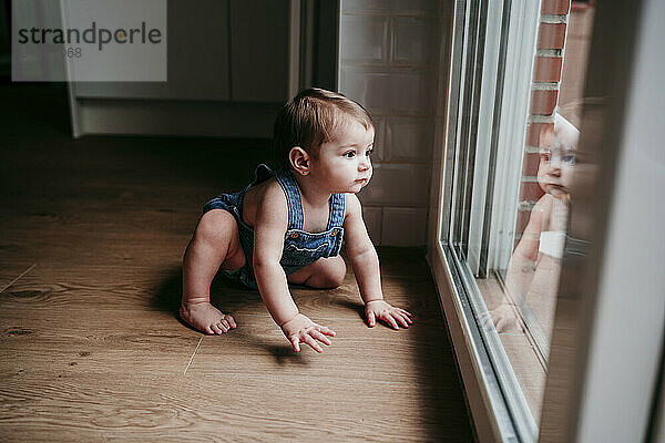 Cute baby girl sitting near window at home