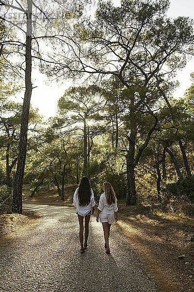 Teenage girl walking with mother on road in forest at sunset