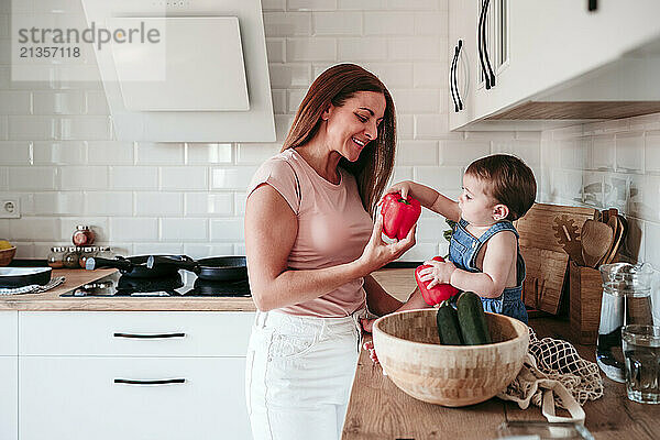 Smiling mother with daughter holding vegetable in kitchen at home