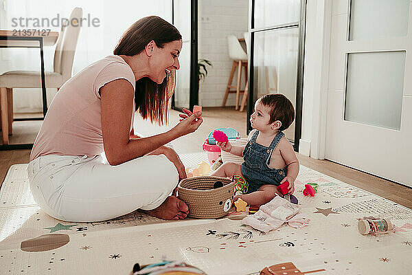 Happy mother and daughter playing with toys sitting on rug at home