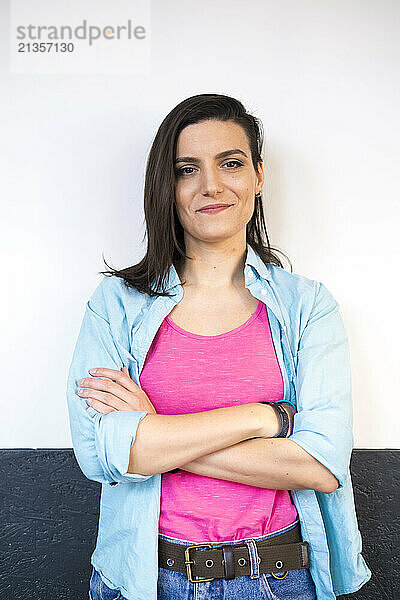 Smiling woman with arms crossed standing in front of wall