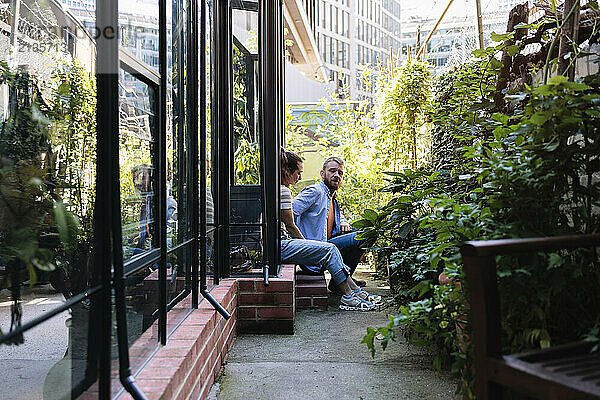 Multiracial couple sitting and discussing near greenhouse