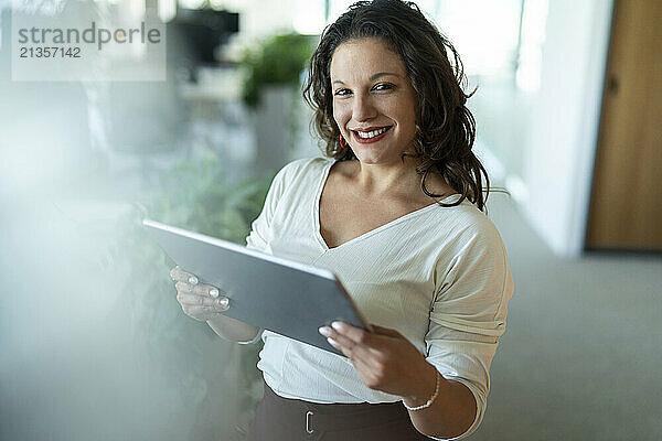 Happy businesswoman wearing smart casual holding digital PC and standing in office