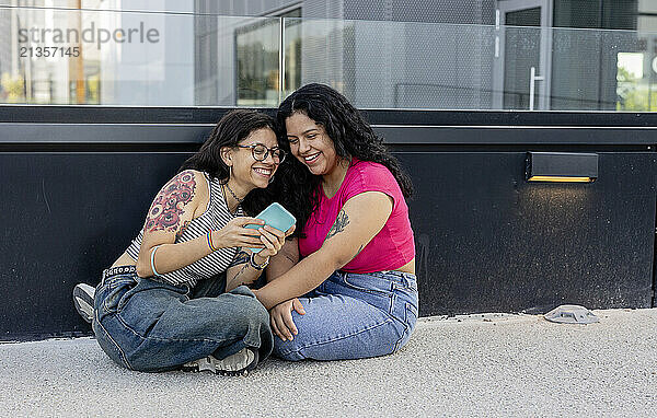 Happy lesbian couple using smart phone and sitting on ground