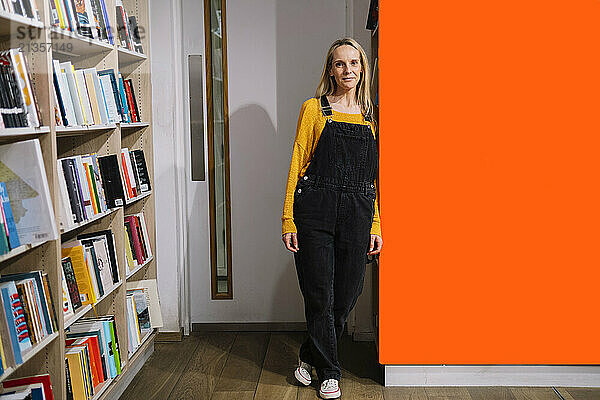 Confident librarian standing by orange wall in library