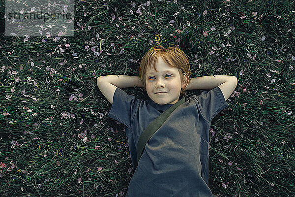 Smiling boy with hands behind head lying on grass