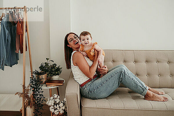 Happy mother and daughter sitting on sofa in living room at home