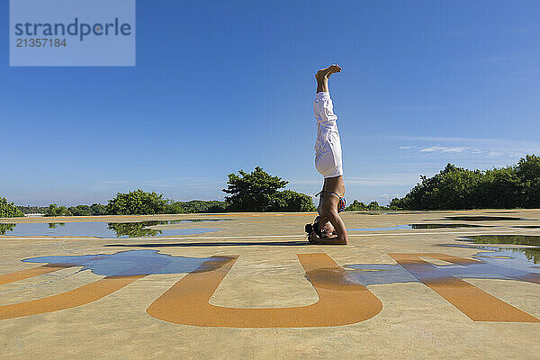 Woman doing headstand on ground at public park under blue sky