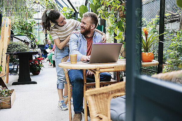 Woman with boyfriend sitting near laptop in greenhouse