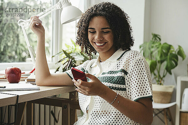 Happy curly haired girl using smart phone at desk