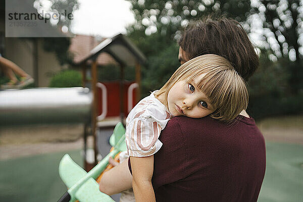 Tired girl resting on her father's shoulder at park