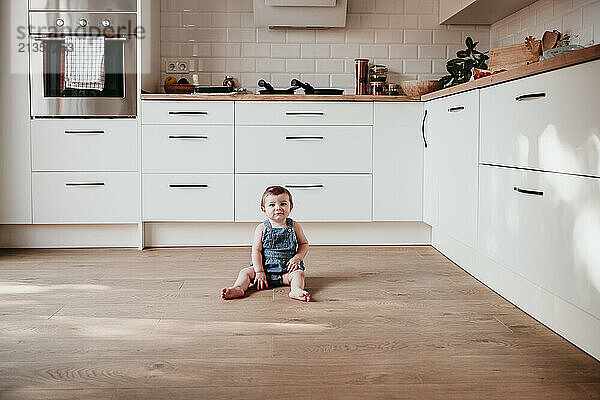 Baby girl sitting on floor in domestic kitchen at home