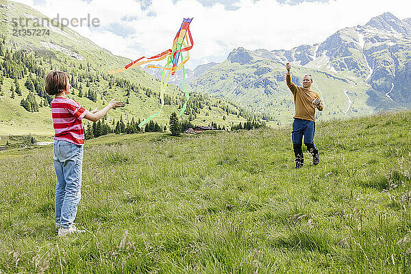 Father and daughter playing with kite on meadow near mountain